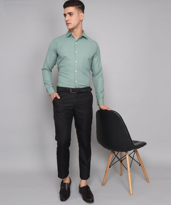 a man in a green shirt and black pants standing next to a chair